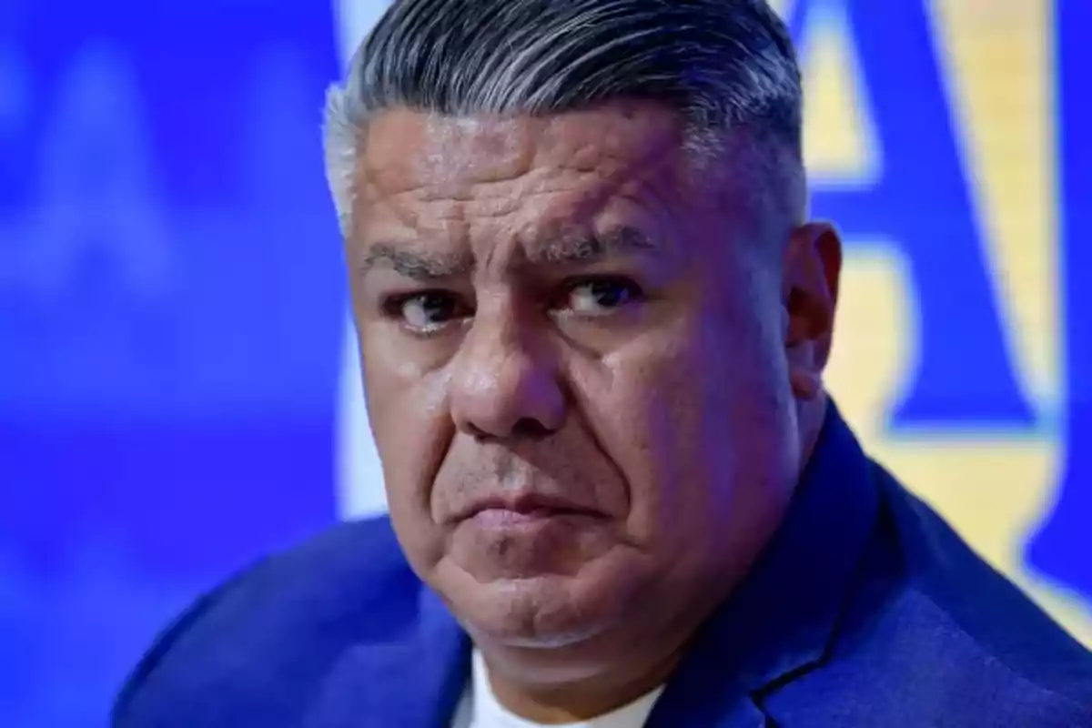 Gray-haired man with a serious expression against a blurred blue and yellow background