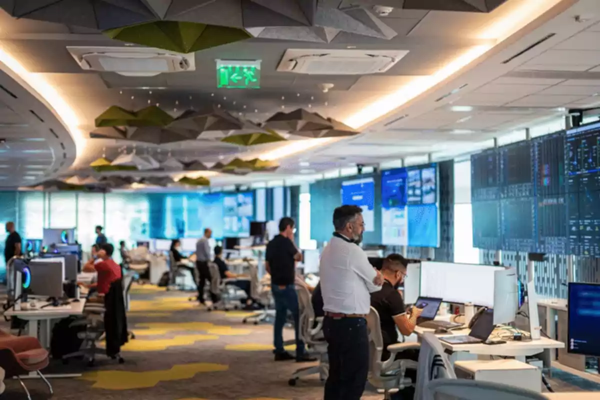People working in a modern office with multiple screens and a geometric ceiling design. People working in a modern office with multiple screens and a geometric ceiling design.