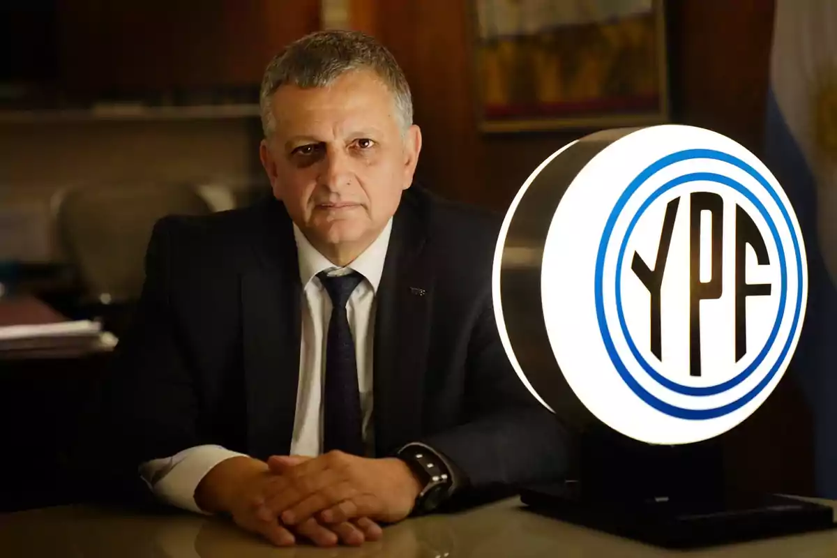 Hombre de traje sentado en una oficina junto a un logo iluminado de YPF Hombre de traje sentado en una oficina junto a un logo iluminado de YPF