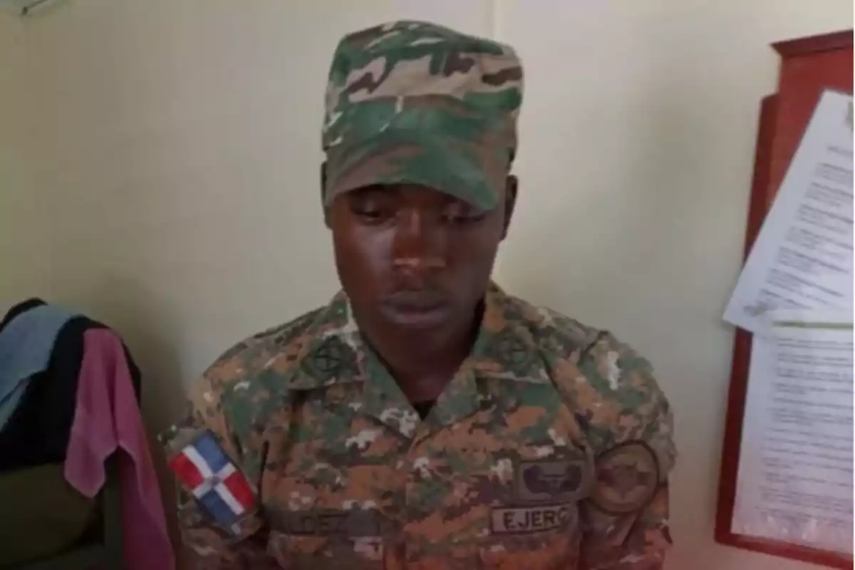 Soldado con uniforme de camuflaje del ejército dominicano mirando hacia abajo en una habitación con paredes claras y documentos en el fondo