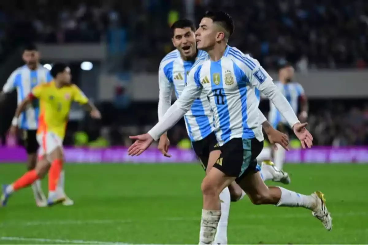 Futbolista argentino celebrando un gol en un partido mientras sus compañeros corren detrás de él y jugadores rivales observan al fondo