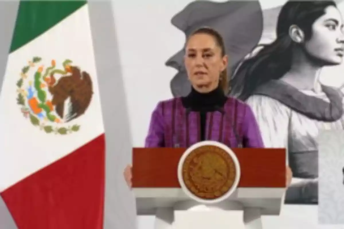 Una persona hablando en un podio con el escudo de México y una bandera mexicana al lado.