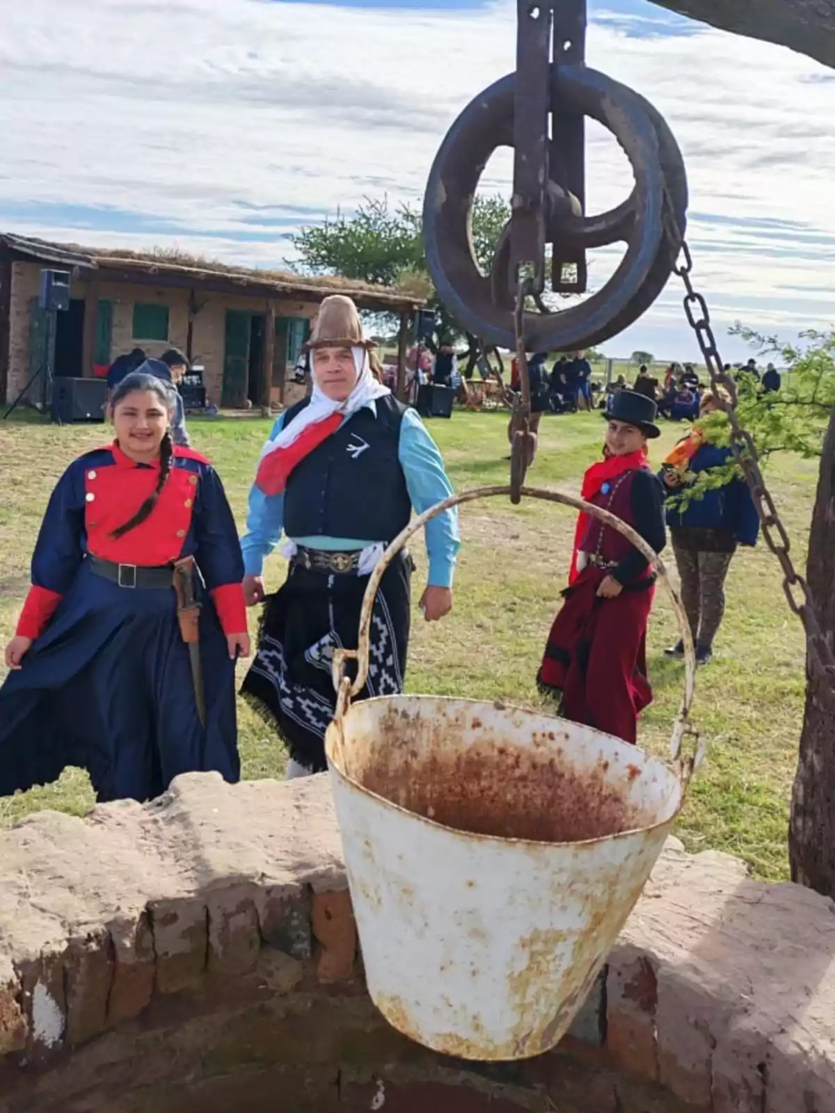 Personas vestidas con trajes tradicionales posan cerca de un pozo con un balde oxidado en un entorno rural. Personas vestidas con trajes tradicionales posan cerca de un pozo con un balde oxidado en un entorno rural.