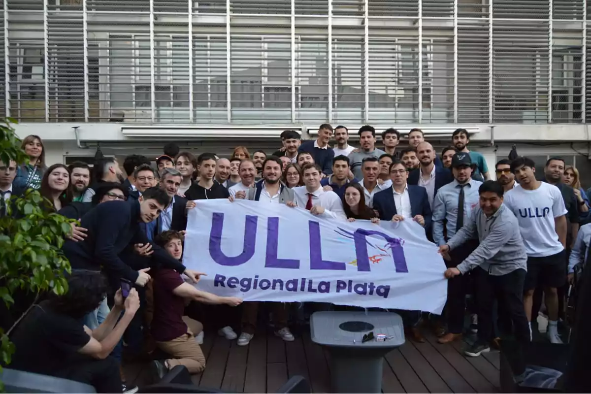 Un grupo de personas posando con una pancarta que dice "ULL Regional La Plata" frente a un edificio.