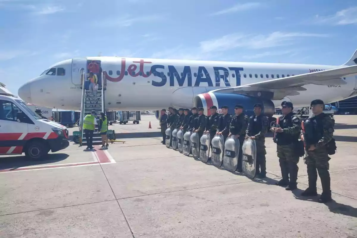 Un avión de JetSMART en el aeropuerto con personal de seguridad alineado y una ambulancia cercana.