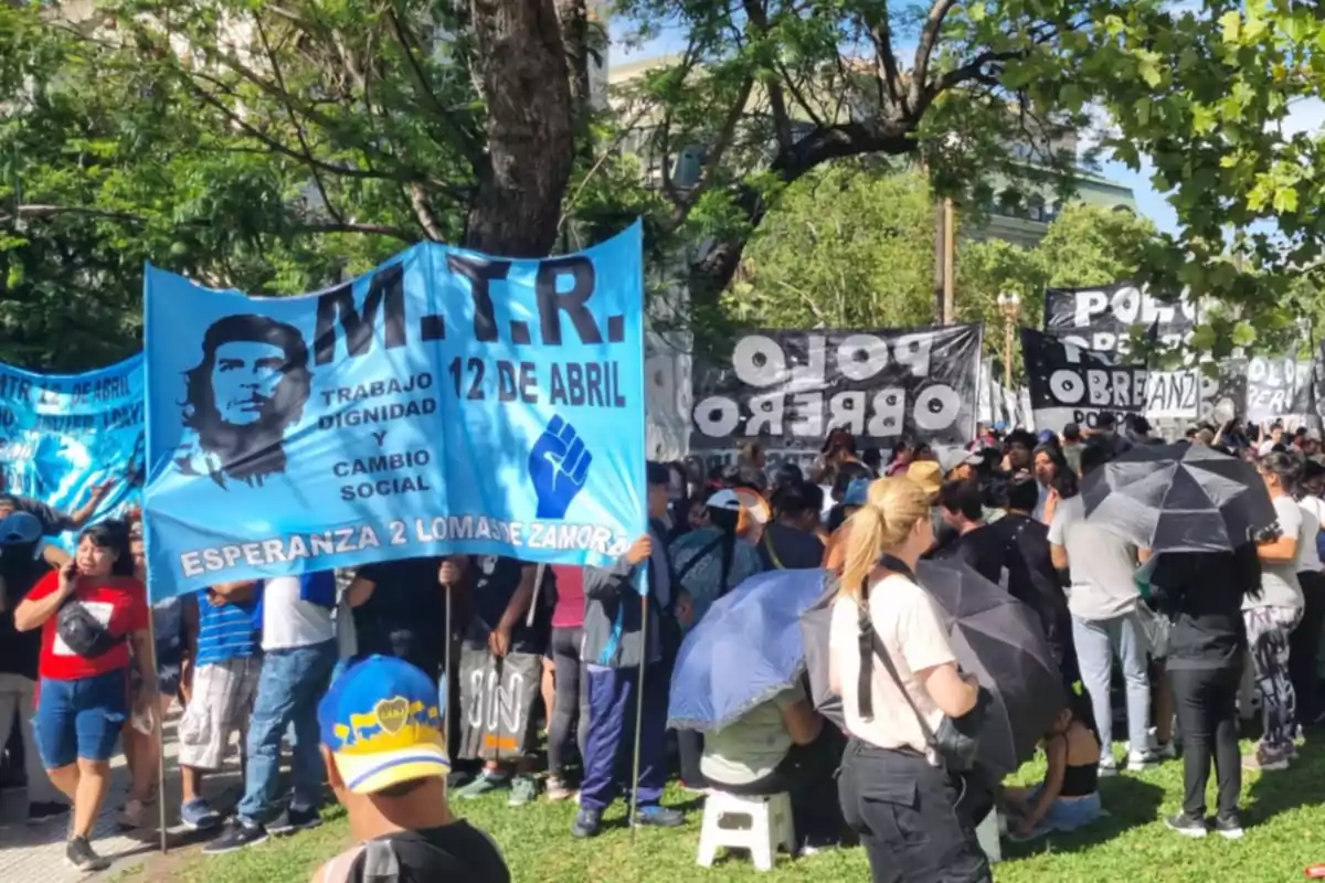 Un grupo de personas se reúne en un parque sosteniendo pancartas de colores con mensajes de trabajo, dignidad y cambio social.