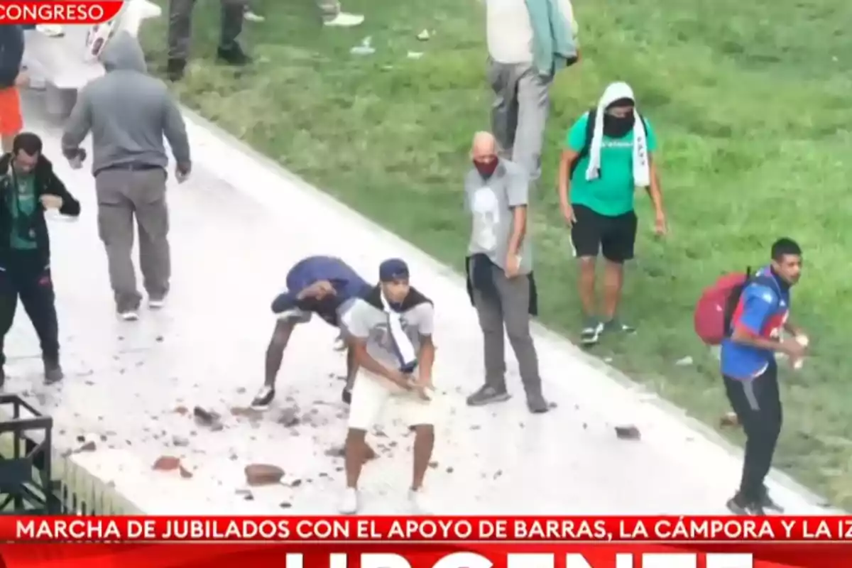 Un grupo de personas en una manifestación, algunas con el rostro cubierto, en un área con césped y pavimento.