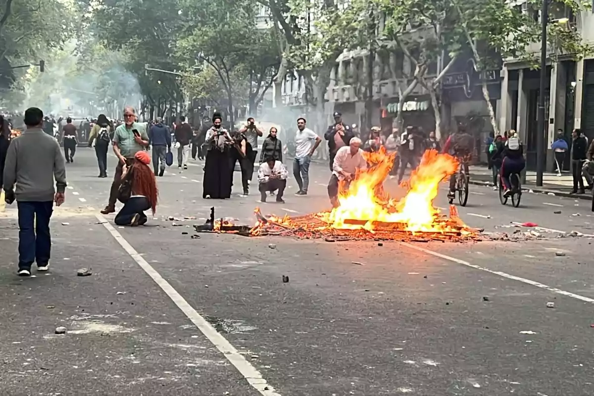 Personas en una calle con una barricada en llamas y humo en el ambiente.