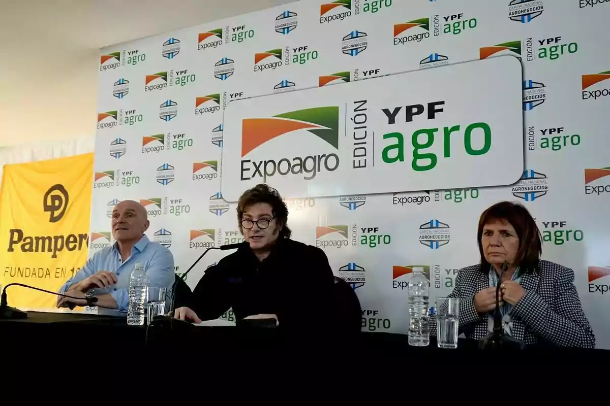 Tres personas sentadas en una mesa con micrófonos y botellas de agua frente a un fondo con logotipos de Expoagro y YPF Agro.