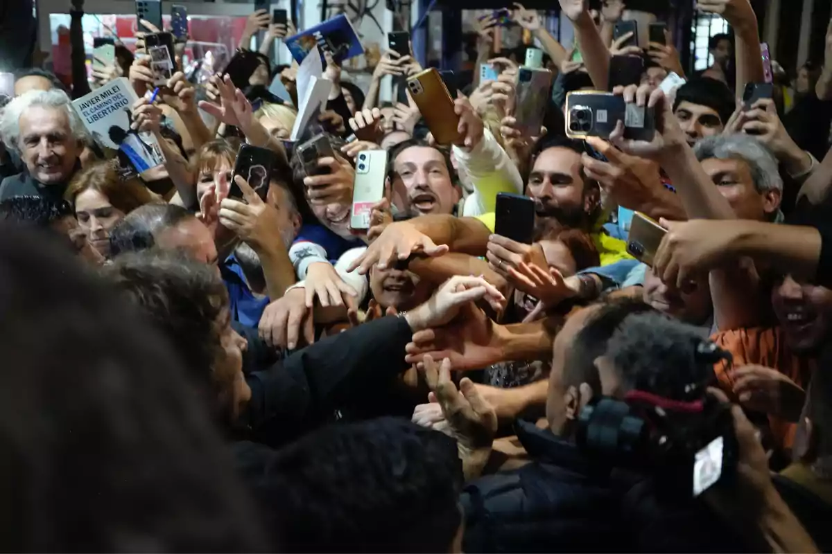 A group of people crowds around someone, raising their phones and hands in an atmosphere of excitement and enthusiasm. A group of people crowds around someone, raising their phones and hands in an atmosphere of excitement and enthusiasm.