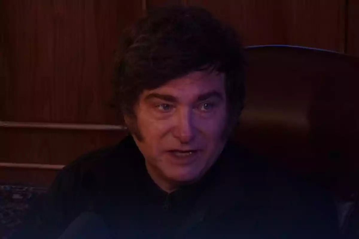 Un hombre con cabello oscuro y expresión seria en un ambiente con iluminación tenue.