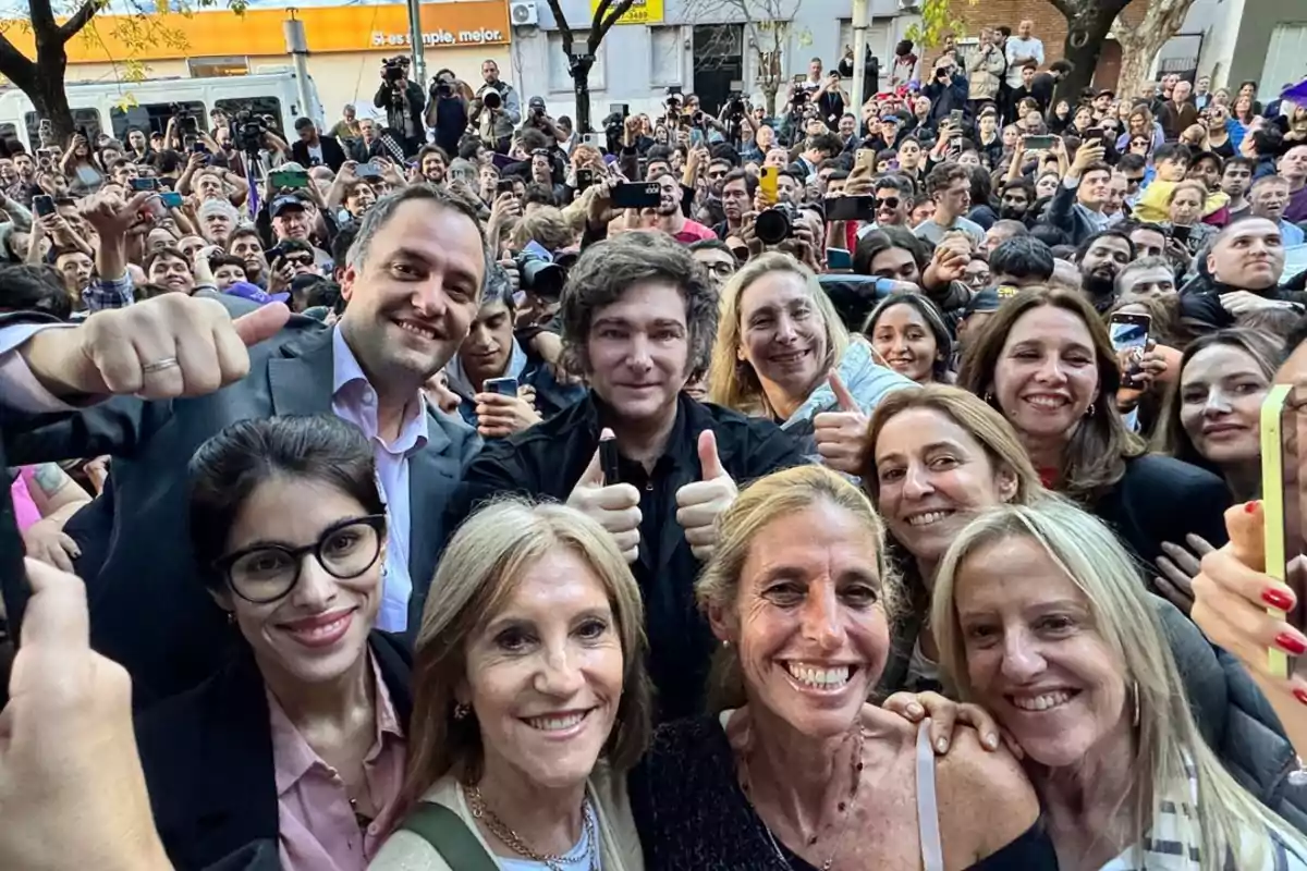 Un grupo de personas sonríe y posa para una selfie en medio de una multitud.