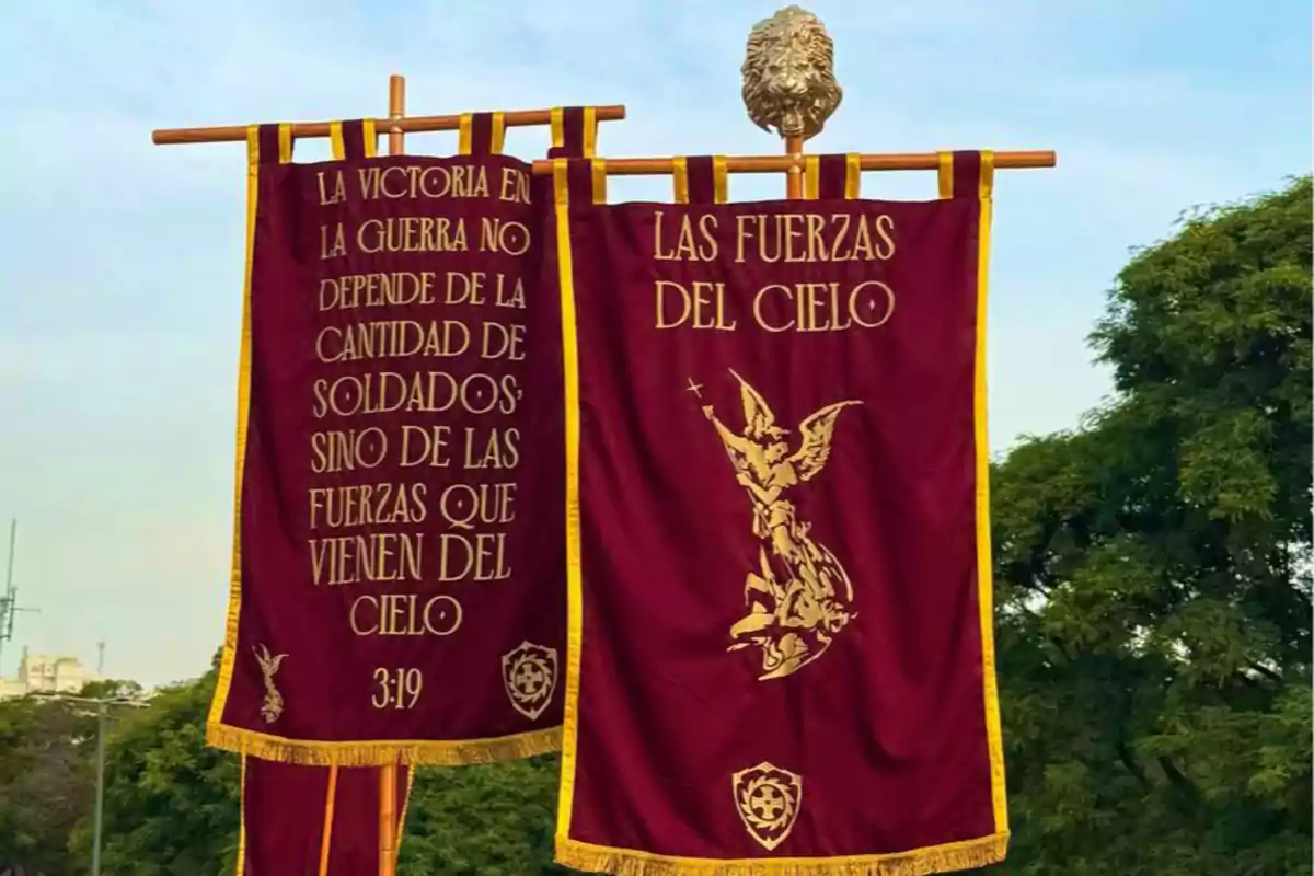 Banderas rojas con bordes dorados y texto religioso en un entorno al aire libre.