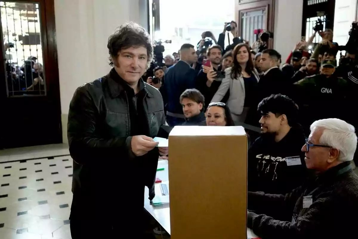 Una persona emitiendo su voto en un centro de votación rodeado de periodistas y observadores.