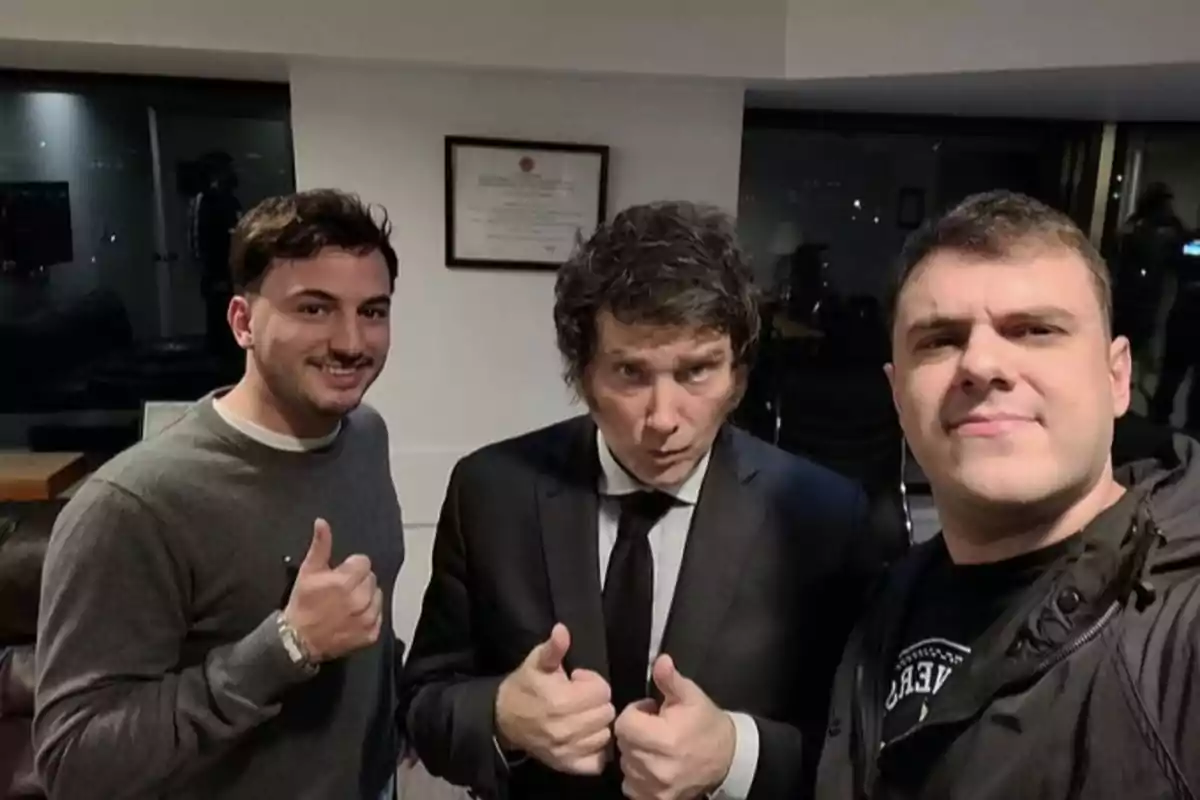 Three men pose for a photo in an office, two of them giving a thumbs-up gesture, and the one in the center wearing a suit and tie. Three men pose for a photo in an office, two of them giving a thumbs-up gesture, and the one in the center wearing a suit and tie.