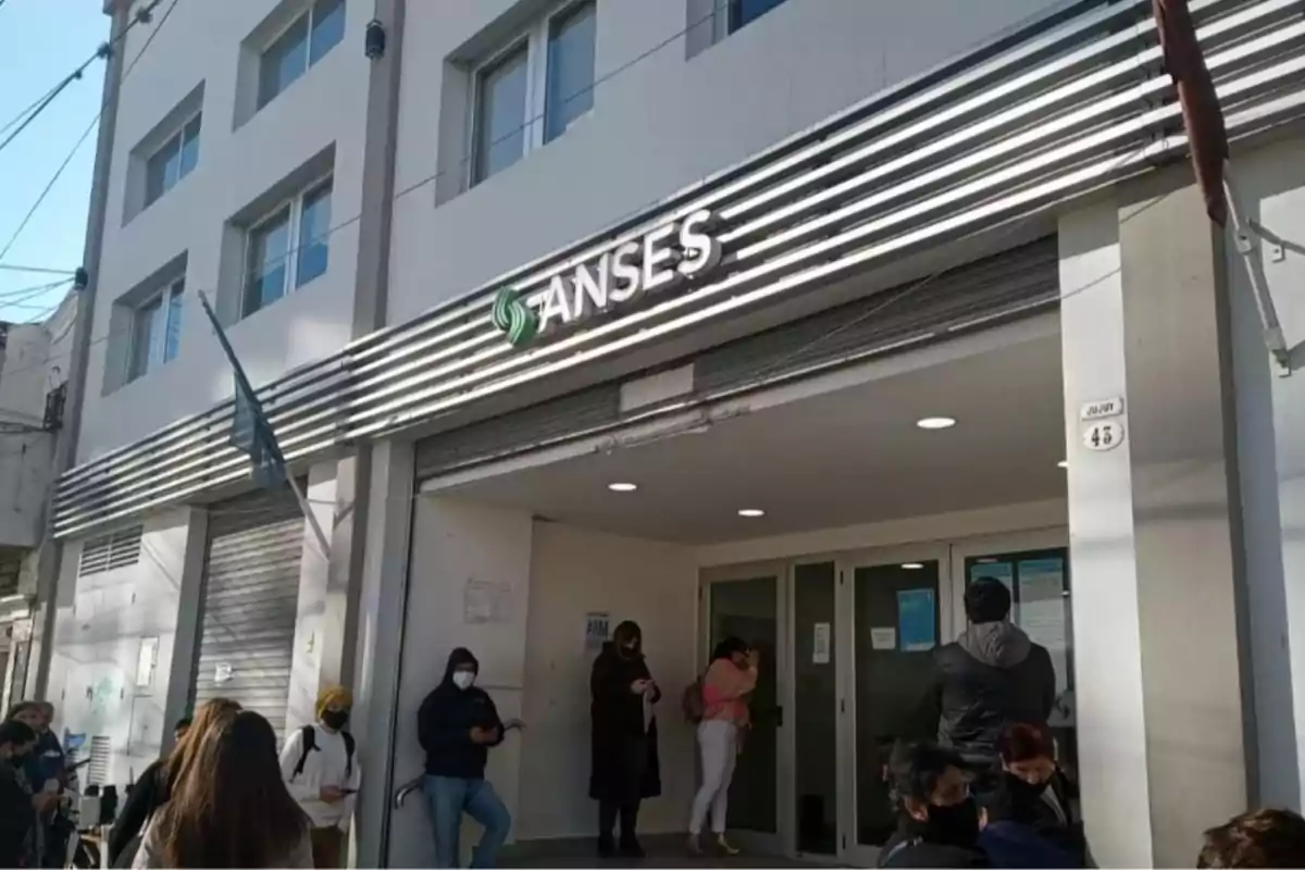 Personas haciendo fila en la entrada de una oficina de ANSES en un edificio blanco