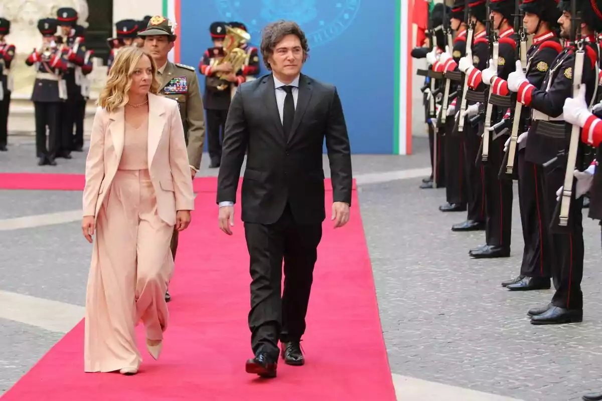 Two people walk on a red carpet while being escorted by a uniformed honor guard. Two people walk on a red carpet while being escorted by a uniformed honor guard.