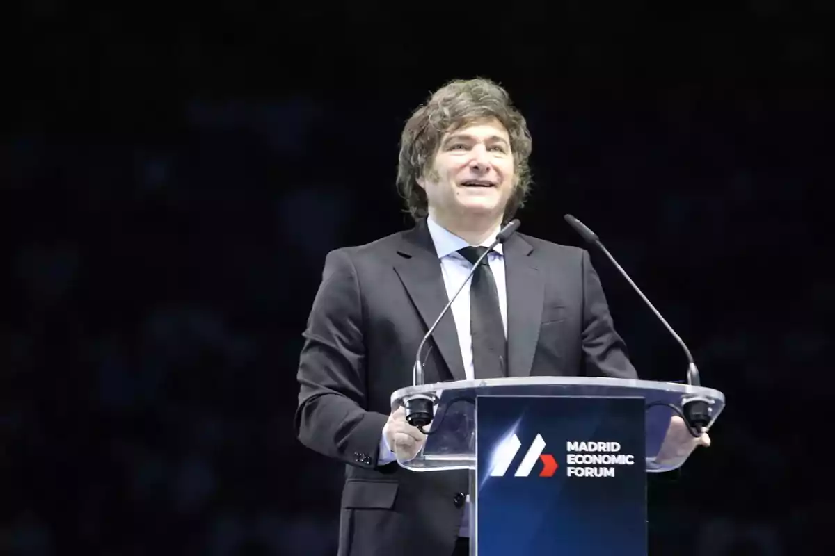 Brown-haired man in a dark suit speaking at a podium with the Madrid Economic Forum logo Brown-haired man in a dark suit speaking at a podium with the Madrid Economic Forum logo