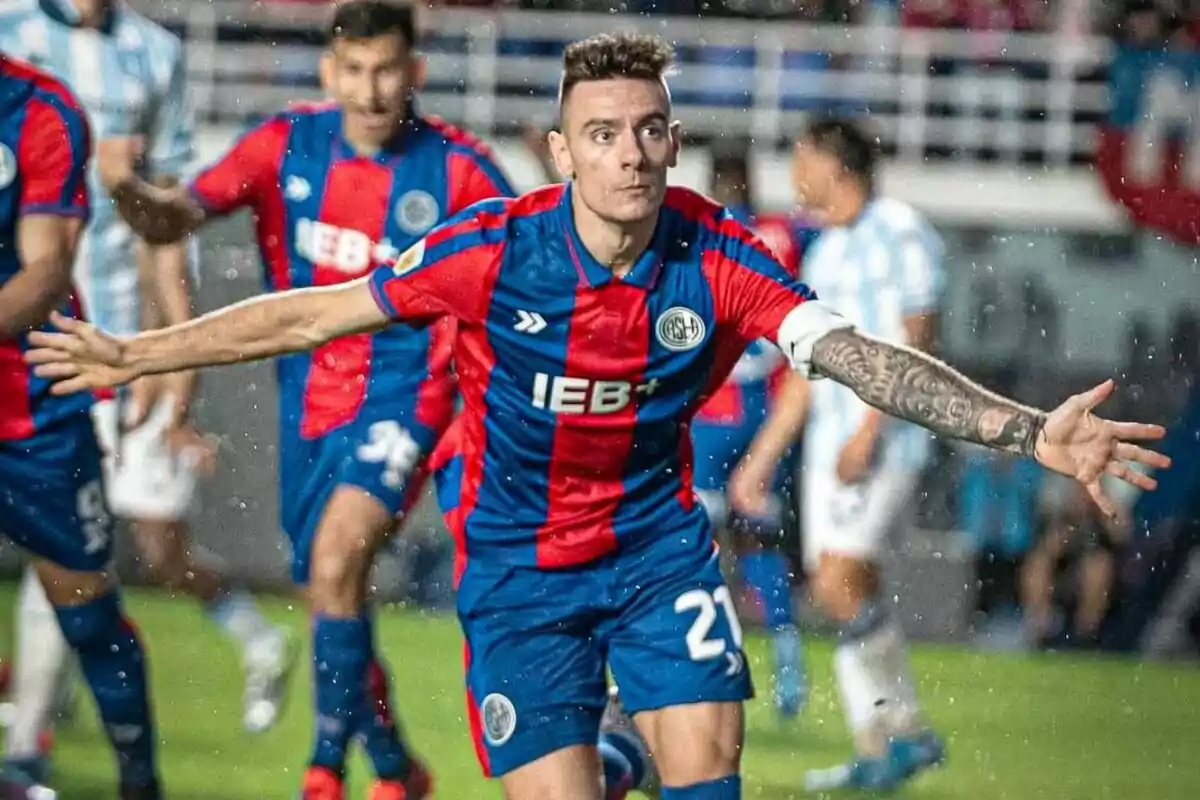 Futbolista con uniforme azul y rojo celebrando un gol con los brazos extendidos en un estadio durante un partido Futbolista con uniforme azul y rojo celebrando un gol con los brazos extendidos en un estadio durante un partido