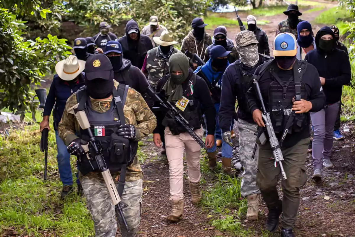 A group of armed and masked people walks along a path surrounded by vegetation.