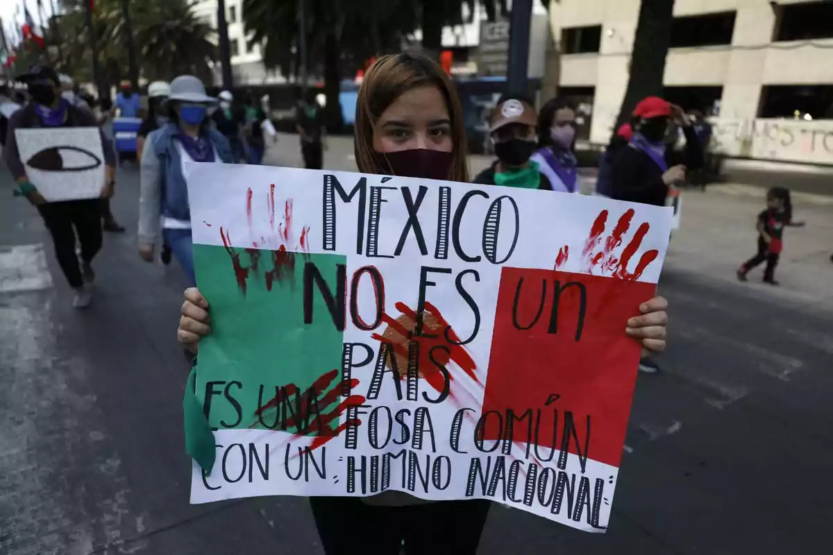 Una persona sostiene un cartel en una manifestación, con un mensaje crítico sobre la situación en México, rodeada de otras personas que también participan en la marcha.