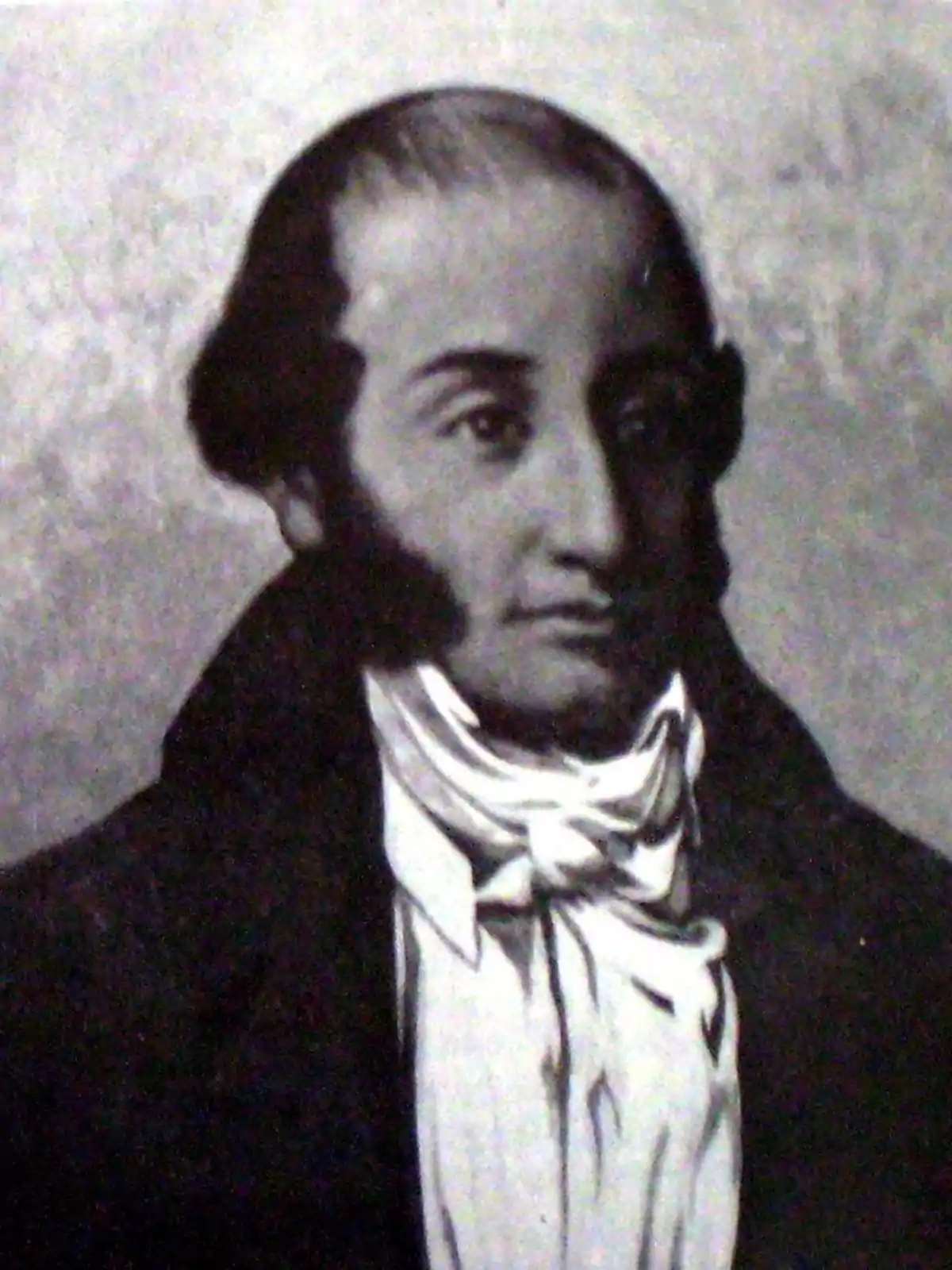 Retrato en blanco y negro de un hombre con cabello oscuro y patillas, vistiendo una chaqueta oscura y una camisa con cuello alto y pañuelo. Retrato en blanco y negro de un hombre con cabello oscuro y patillas, vistiendo una chaqueta oscura y una camisa con cuello alto y pañuelo.
