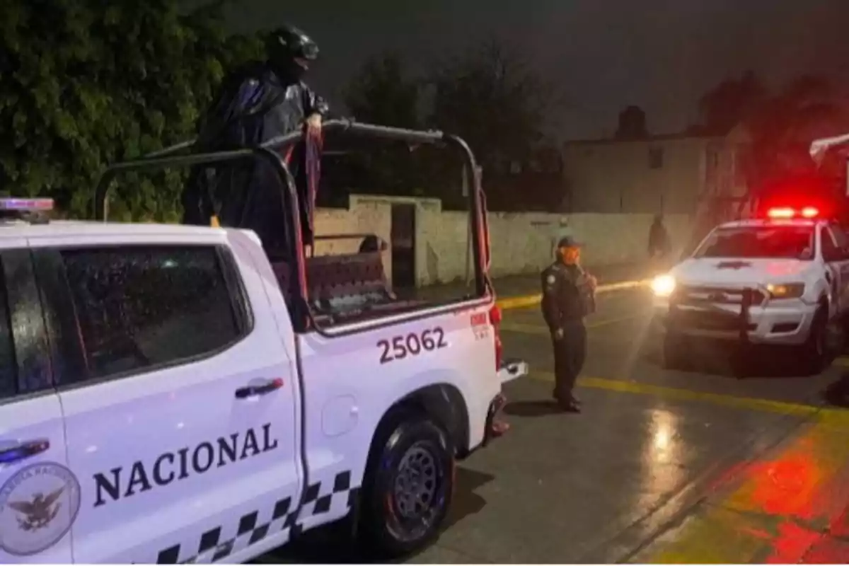 Una patrulla de la Guardia Nacional en una calle oscura con un agente de pie junto a ella y una persona vestida de negro en la parte trasera del vehículo.