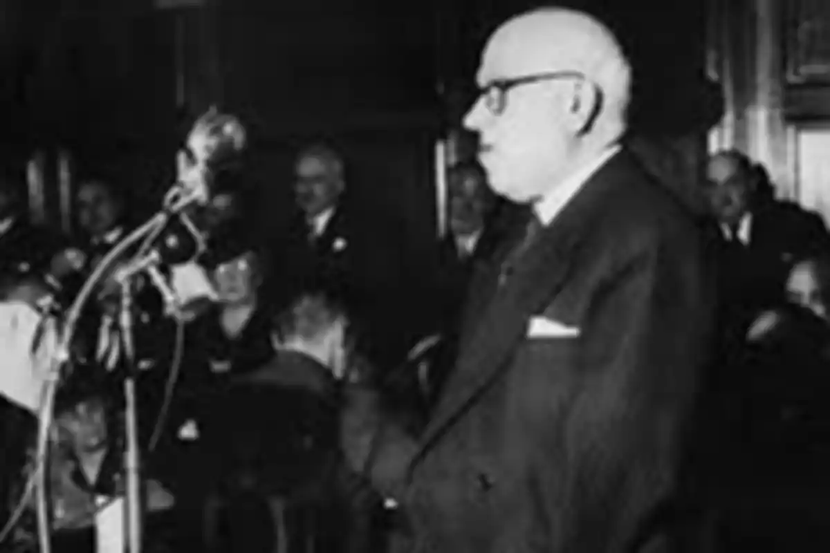 Older man standing, wearing glasses and a dark suit, speaking in front of a microphone in a room full of people Older man standing, wearing glasses and a dark suit, speaking in front of a microphone in a room full of people
