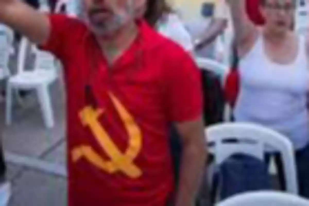 Man wearing a red t-jersey with a communist symbol raising his arm at an outdoor event with white plastic chairs Man wearing a red t-jersey with a communist symbol raising his arm at an outdoor event with white plastic chairs