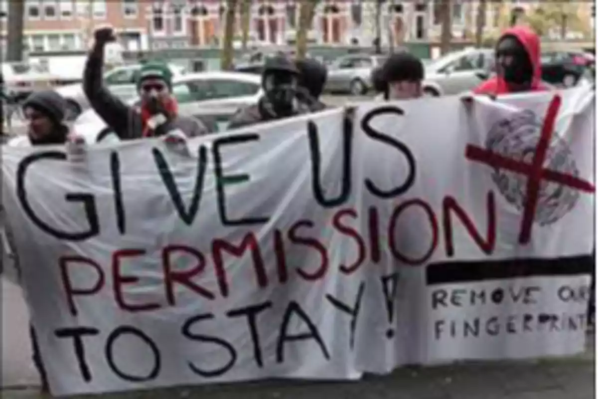 Varias personas sostienen una pancarta que pide permiso para quedarse y eliminar huellas dactilares durante una protesta en la calle. Varias personas sostienen una pancarta que pide permiso para quedarse y eliminar huellas dactilares durante una protesta en la calle.