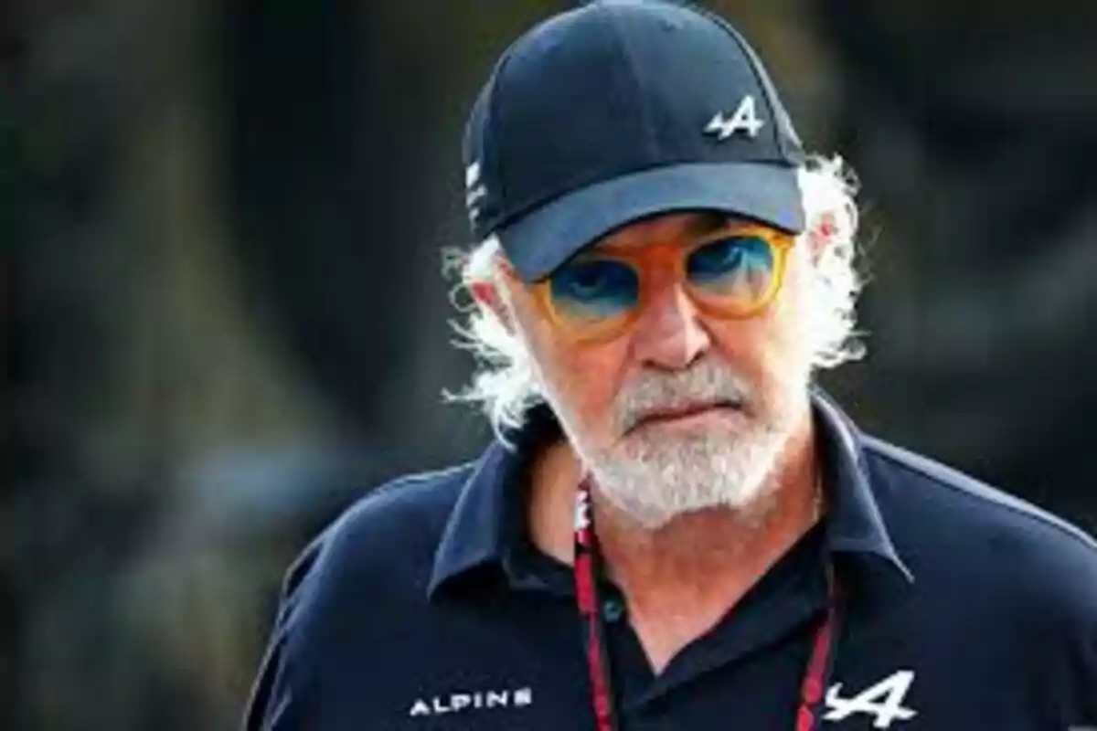 Hombre de cabello canoso y barba con gafas de sol coloridas y gorra negra de la escudería Alpine