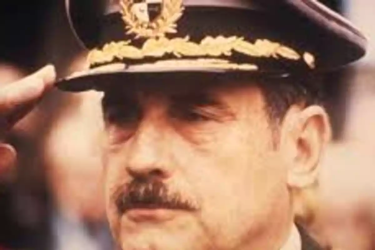 Hombre con bigote usando un uniforme militar y gorra con insignias doradas mientras saluda Hombre con bigote usando un uniforme militar y gorra con insignias doradas mientras saluda