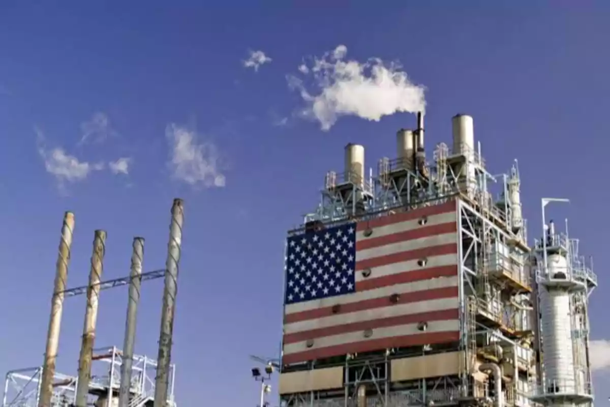 Planta industrial con chimeneas y una gran bandera de Estados Unidos en la estructura bajo un cielo azul.