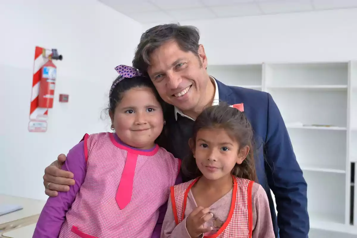 Un hombre sonriente posa con dos niñas en un aula.