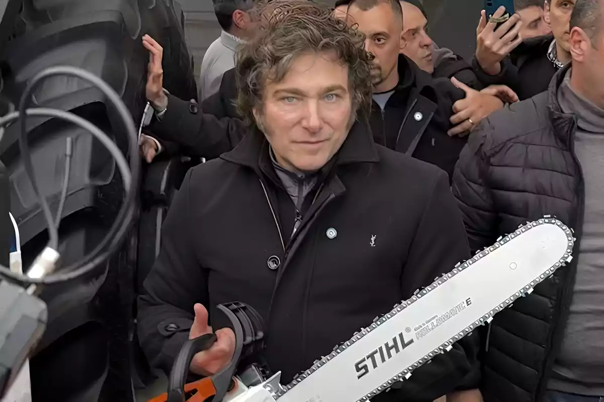 A man with curly hair holds a chainsaw surrounded by several people.