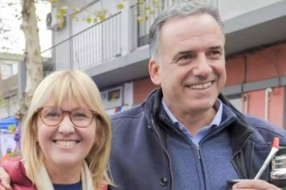 Dos personas sonriendo al aire libre, una de ellas sostiene un mate.