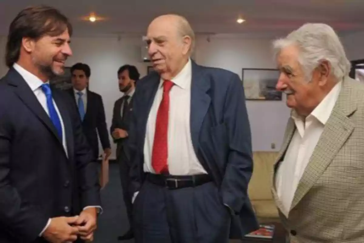 Tres hombres conversando y sonriendo en un ambiente formal.