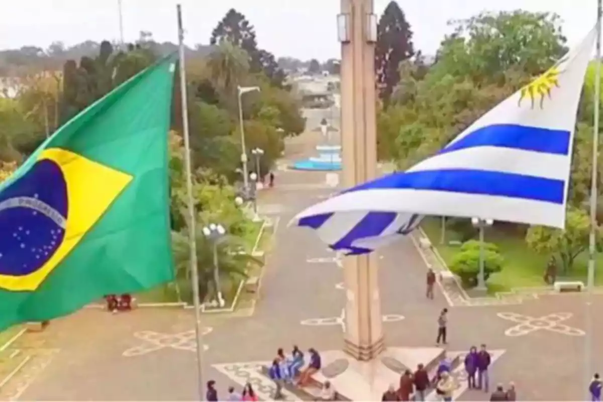 Banderas de Brasil y Uruguay ondeando en una plaza con personas reunidas alrededor de un monumento central.