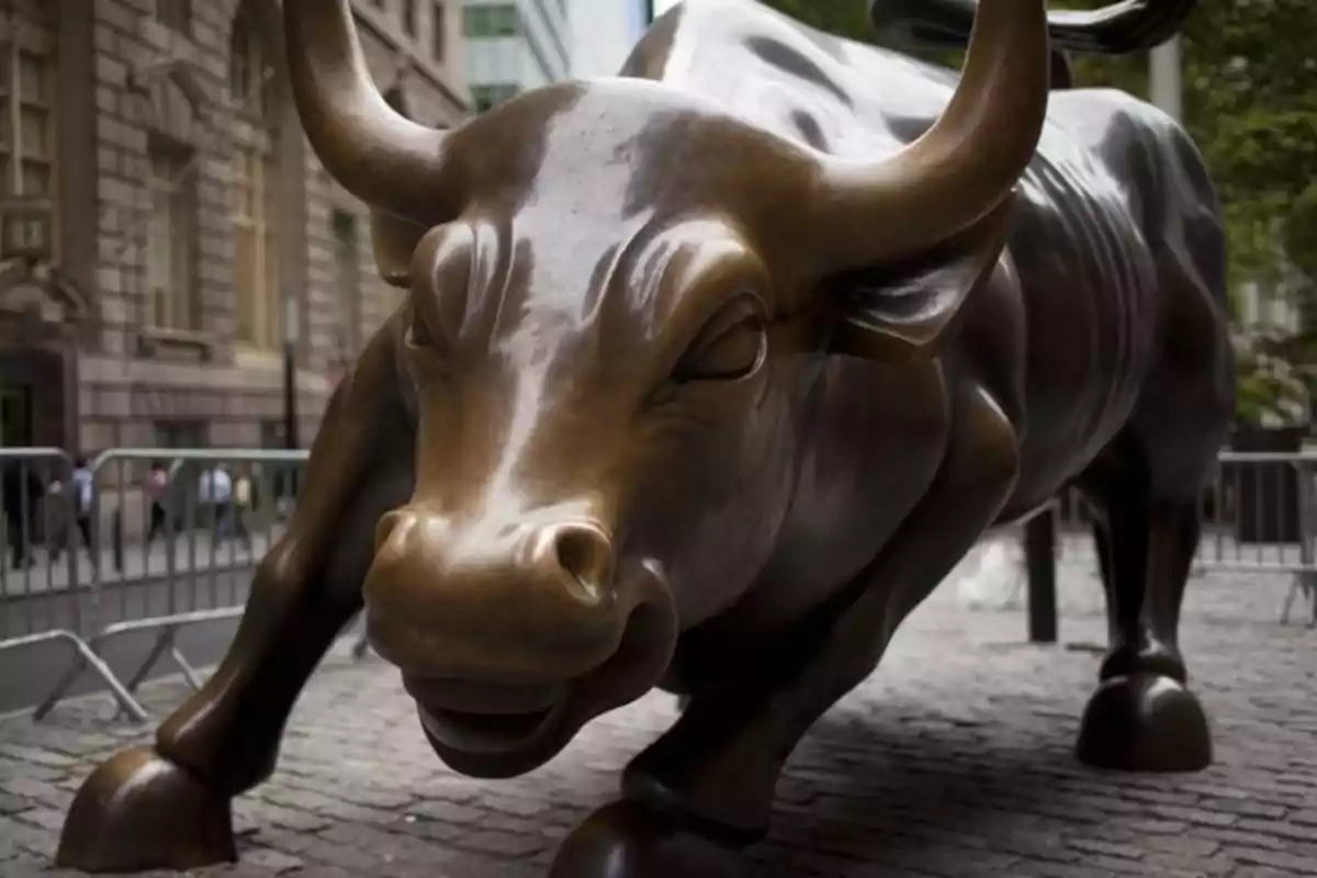 Sculpture of a bronze bull on a street surrounded by buildings and metal barriers.