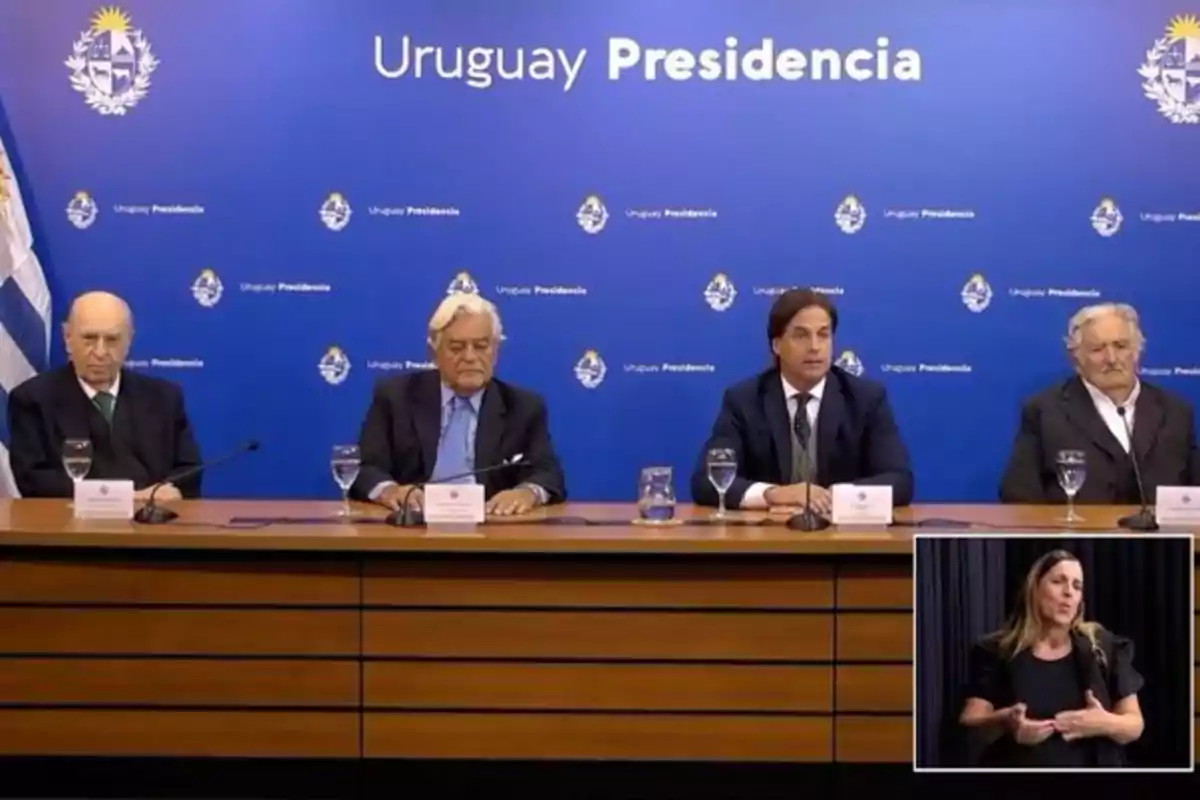 Un grupo de personas sentadas en una mesa frente a un fondo azul que dice 