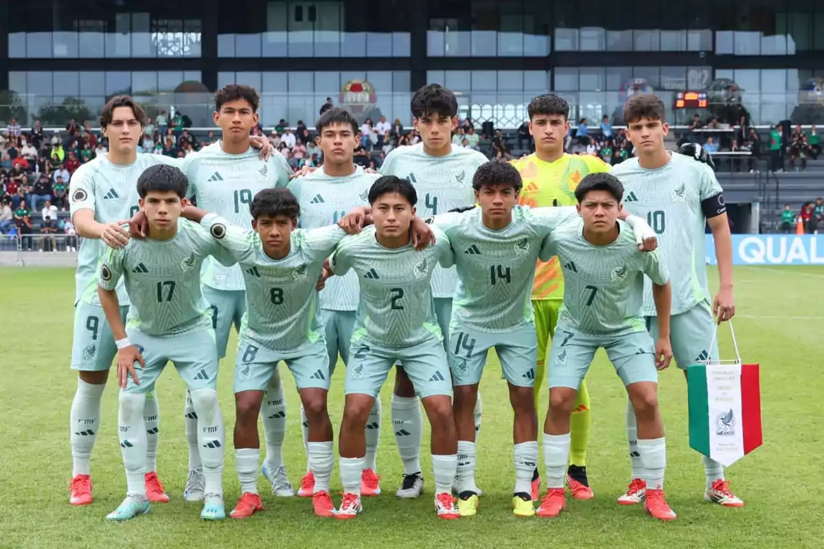 Un equipo de fútbol juvenil posa para una foto grupal en el campo antes de un partido, con jugadores vistiendo uniformes verdes y un estadio lleno de espectadores al fondo.