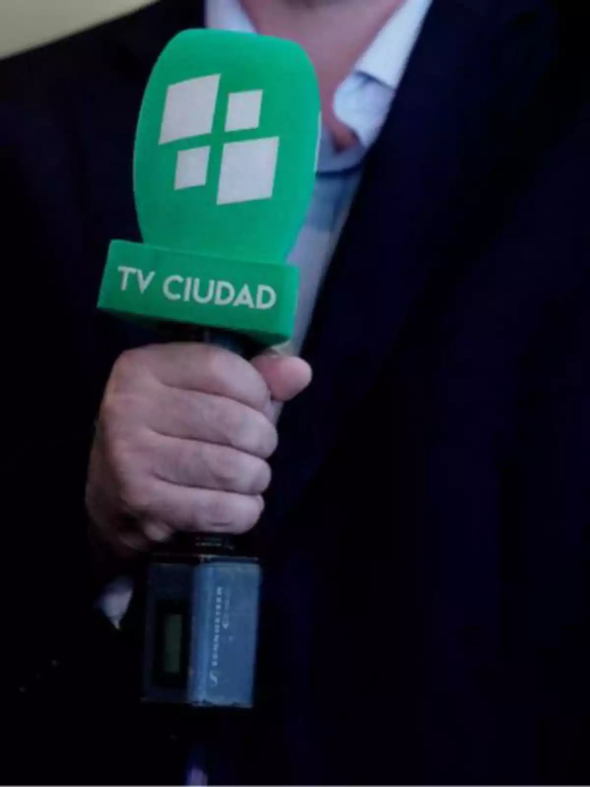 A person holding a green microphone with the TV Ciudad logo.