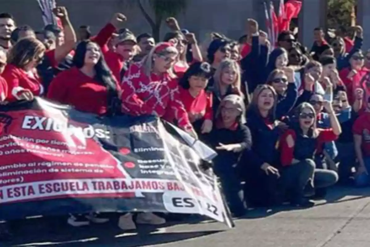 Un grupo de personas vestidas de rojo y negro sostiene una pancarta durante una manifestación, levantando los puños en señal de protesta.