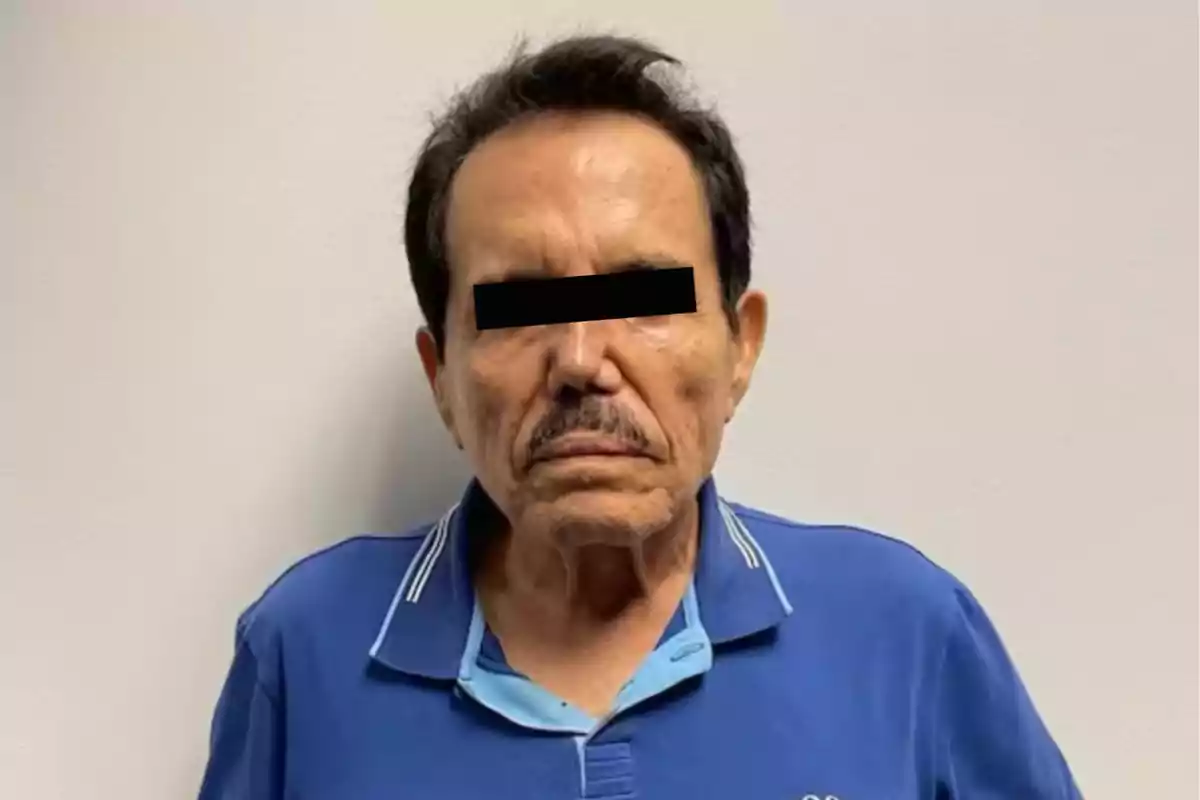 Un hombre de pie con una camisa azul y los ojos cubiertos por una franja negra.