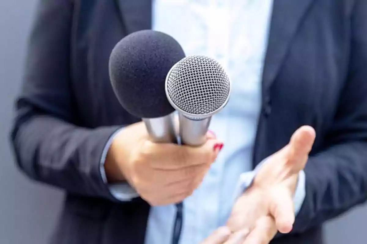 Person holding two microphones in one hand while gesturing with the other.