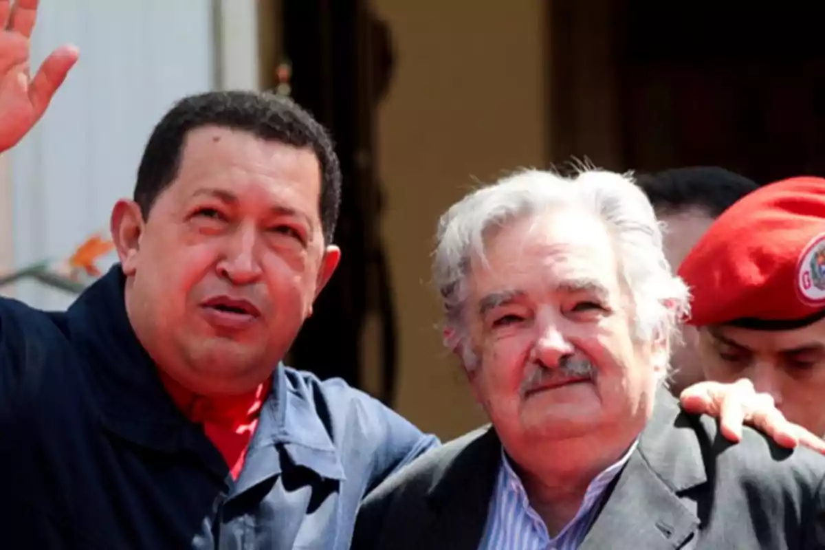 Dos hombres posan juntos mientras uno de ellos levanta la mano en señal de saludo.