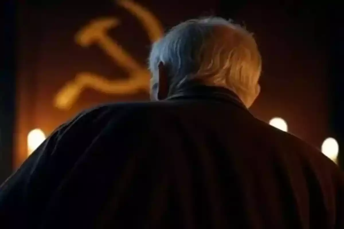 A man with his back turned in front of a hammer and sickle symbol illuminated by candles. A man with his back turned in front of a hammer and sickle symbol illuminated by candles.