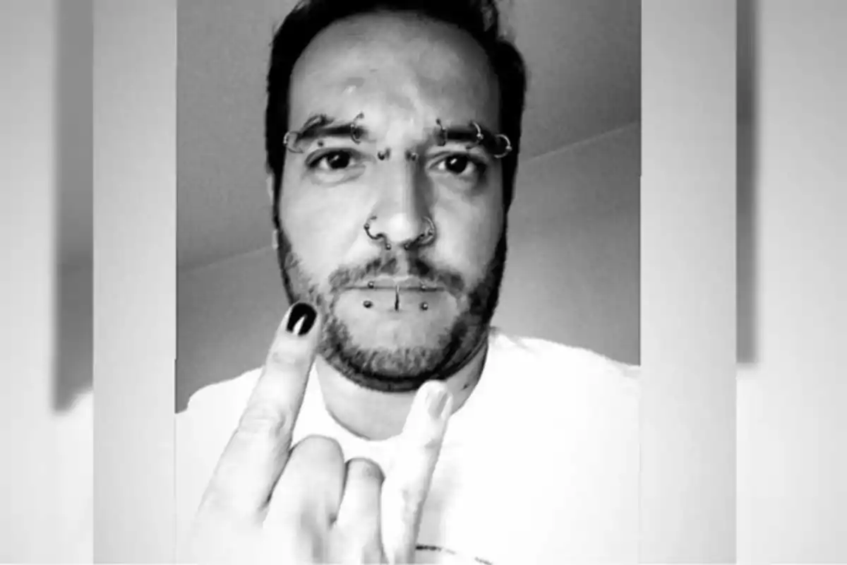 Man with several facial piercings making the horns gesture with his hand and one fingernail painted black