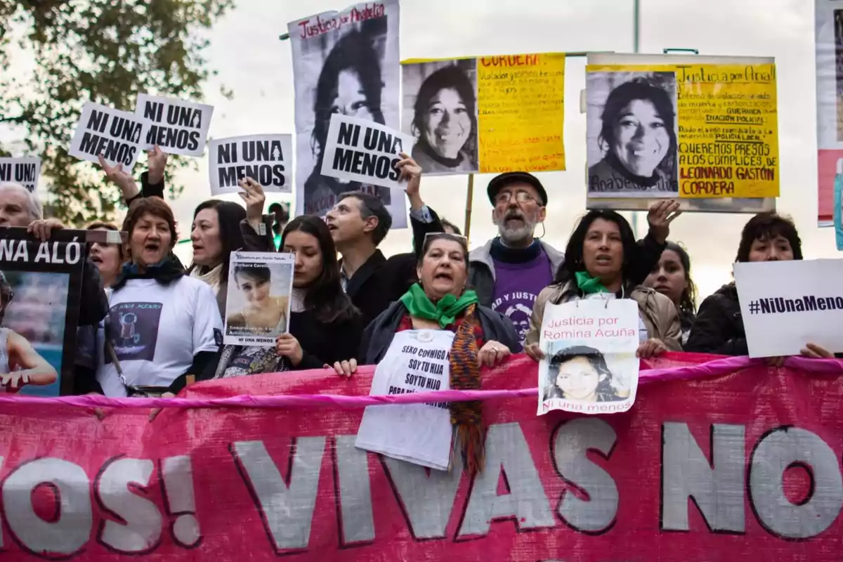 Grupo de personas manifestándose con pancartas y carteles que dicen Ni una menos y exigen justicia por víctimas de feminicidio, sosteniendo una gran manta rosa