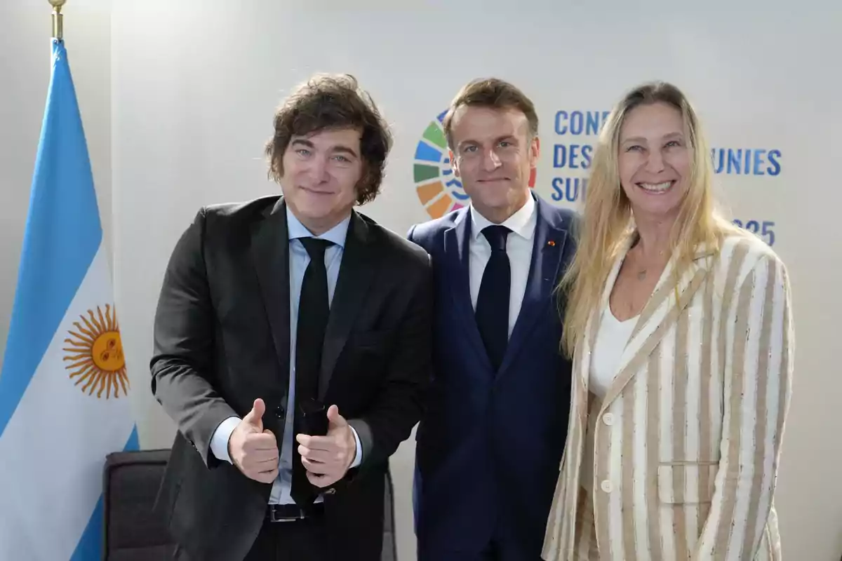 Tres personas vestidas de manera formal posan sonrientes junto a una bandera de Argentina y un cartel de fondo